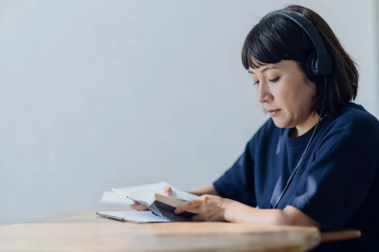 Uma pessoa autista de nível 1, com fones de ouvido, concentrada em um livro em uma mesa.