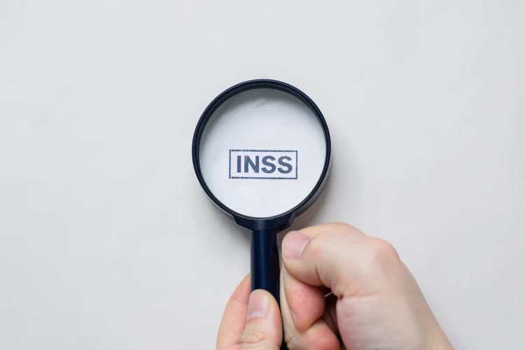 Uma mão segurando uma lupa sobre um documento com selo do INSS.