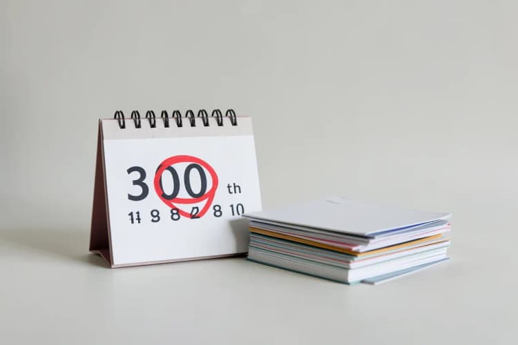 Um calendário com o dia 30 marcado com um círculo vermelho, ao lado de uma pilha de papéis.